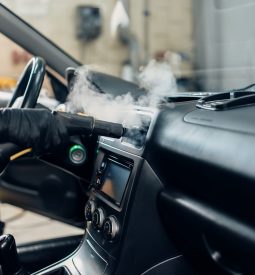 Carwash service, male worker in gloves removing dust and dirt with steam cleaner. Professional dry cleaning of car interior